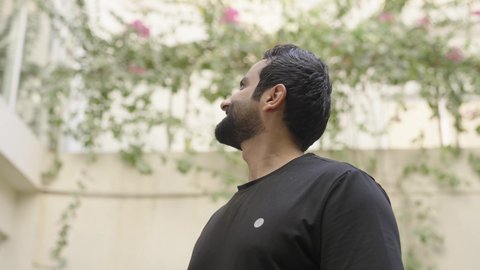 Gestures of happiness and joy, spending enjoyable times outdoors, parks and public gardens, an Arab Gulf Saudi man wearing casual attire walking in one of the gardens and looking up, enjoying the fresh air and flowers.