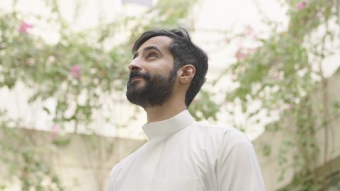 المنتزهات والحدائق العامة، قضاء أوقات ممتعة فى الهواء الطلق، رجل عربي خليجي سعودي يرتدي الثوب الابيض يقوم بالمشي فى احد الحدائق و ينظر الى الاعلي ، الاستمتاع بالهواء الطلق والزهور