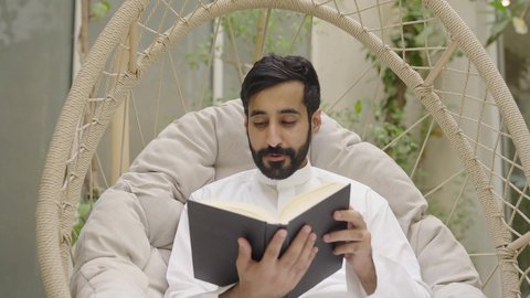 مفهوم التعلم والتثقف الذاتي، تصوير مقرب لرجل عربي خليجي سعودي يرتدي الثوب التقليدي يجلس في الهواء الطلق يقوم بقراءة كتاب، قضاء وقت ممتع مع النفس، تنمية الذخيرة اللغوية