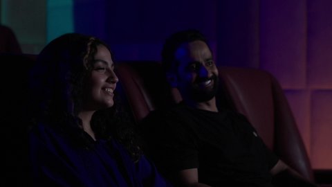 Watching movies and theater shows in the cinema, a Saudi Arabian couple dressed in casual attire sitting in the cinema hall, expressions indicating happiness, recreational activities, spending enjoyable times, weekend.