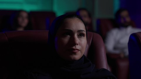 الاثارة والتشويق والاندماج، مشاهدة الأفلام المرعبه والعروض المسرحية في السينما، تعابير الخوف والذعر ، قضاء أوقات ممتعة، امراة عربيه خليجيه سعودية محجبه ترتدي العباءة تجلس في صالة السينما