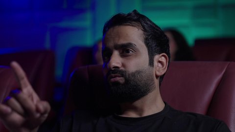 الاشارة الى شيء ما، مشاهدة الأفلام والمسرحيات والعروض المتنوعة, شاشات ضوئية كبيرة لزيادة الاستمتاع بالتجربة، القيام بنشاطات ترفيهية ممتعة, رجل عربي خليجي سعودي يرتدي الزي الكاجوال يجلس في قاعة السينما يتابع الفيلم بايماءات الاندماج و التركيز, دور العرض الحديثة في المملكة العربية السعودية