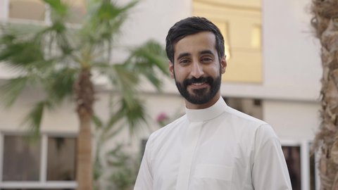 الأناقة والرجولة والوسامة، الاهتمام بالمظهر الخارجي ، تصوير مقرب لشاب عربي خليجي سعودي يرتدي الثوب التقليدي ينظر إلى الكاميرا بإيماءات السعادة والسرور، الاستمتاع بقضاء وقت ممتع فى الهواء الطلق