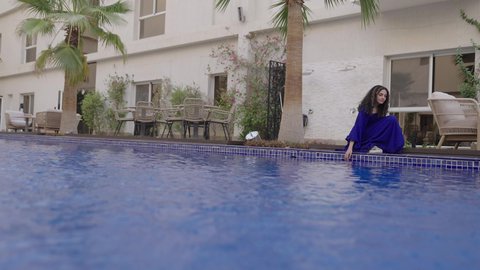 الاستمتاع في إحدى مسابح المملكة، استخدام الاجهزة التقنية الحديثة، الجلوس على حدود البركة المائية ، رحلة سياحية ترفيهية ، عطلة صيفية سعيدة، تصوير لبنت عربيه خليجيه سعودية ترتدي الفستان الازرق تلتقط صورة سيلفي عبر الهاتف المحمول