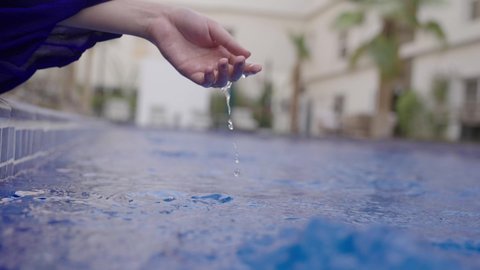 Happy summer vacation, sitting by the edge of the water pool, a recreational tourist trip, a close-up shot of the hand of a Saudi Gulf Arab girl putting her hands in the water, enjoying one of the pools in the Kingdom.