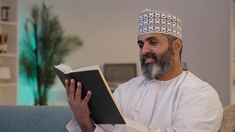 الإهتمام بالعلم و الثقافة, تمضية وقت الفراغ بالتعلم و التثقيف الذاتي، قراءة الرواية والقصة، تعابير التركيز و الاستمتاع، رجل شايب عربي خليجي عماني مبتسم يرتدي الدشداشة و الكمة يمسك بيده كتاب