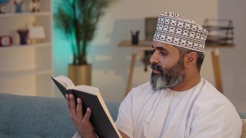 أهمية التثقيف الذاتي، الإهتمام بالعلم و الثقافة, تمضية وقت الفراغ بالتعلم، قراءة الرواية والقصة، تعابير التركيز و الاستمتاع، رجل شايب عربي خليجي عماني مبتسم يرتدي الدشداشة و الكمة يمسك بيده كتاب