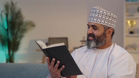 قراءة الكتب و القصص, ثقافة التعلم الذاتي, رجل شايب عربي خليجي عماني مبتسم يرتدي الدشداشة و الكمة يمسك بيده كتاب, إيماءات التركيز و الاندماج, قضاء وقت ممتع