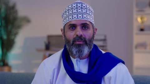 تعابير الفرح و السرور و الحماس للمنافسة، مفهوم الربح و الفوز، ارتداء الأوشحة التشجيعية،  رجل شايب عربي خليجي عماني مبتسم يرتدي الدشداشة و الكمة يضع الوشاح الأزرق و بجانبه كرة القدم