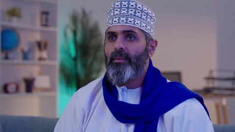 ارتداء الاوشحة التشجيعية، مشاهدة و متابعة المباراة، الحماس والتفاعل مع المنتخب،  رجل شايب عربي خليجي عماني مبتسم يرتدي الدشداشة و الكمة يضع الوشاح الأزرق و يرفع يده بايماءات التشجيع