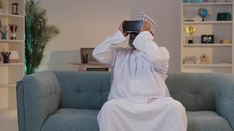 المتعة و التسلية بالمشاهدة عبر نظارات الواقع الافتراضي، محاكاة العالم الخيالي، استخدام جهاز تقني حديث و متطور،  رجل شايب عربي خليجي عماني مبتسم يرتدي الدشداشة و الكمة و يضع نظارة الفي ار ثلاثية الأبعاد