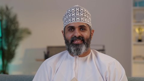 تسويق المنازل و العقارات، النظر الى الكاميرا بايماءات البهجة لامتلاك سكن حديث,   رجل شايب عربي خليجي عماني مبتسم يرتدي الدشداشة و الكمة يحمل بيده مجسم صغير خشبي لمنزل, مفهوم الاسكان و التمليك