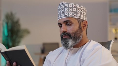 قراءة الكتب بتمعن, الانسجام و الهدوء و السكينة,  رجل شايب عربي خليجي عماني مبتسم يرتدي الدشداشة و الكمة يمسك بيده كتاب,  إيماءات التركيز و الاندماج, قضاء وقت ممتع