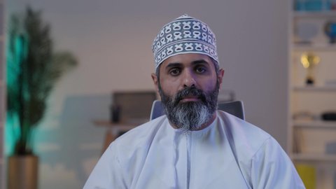 أنشطة ترفيهية ممتعة, قضاء أوقات الفراغ بلعب البلايستيشن,  رجل شايب عربي خليجي عماني مبتسم يرتدي الدشداشة و الكمة يمسك بيده عصا التحكم و يلعب بألعاب الفيديو,  ايماءات التركيز و الاندماج