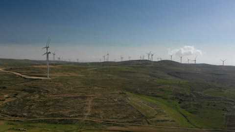 Electricity generation through wind farms, harsh and dry climate, the concept of using renewable energy that is environmentally friendly, sustainable development with alternative energy in Dumat al-Jandal in the Kingdom of Saudi Arabia, aerial drone photography of wind turbine fields and windmills amidst the golden sands in desert areas.
