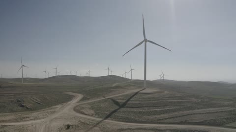 توليد الكهرباء بواسطة مزارع الرياح، مناخ قاسٍ وجاف، مفهوم استخدام الطاقات المتجددة صديقة البيئة، التنمية المستدامة بالطاقة البديلة في دومه الجندل بالمملكة العربية السعودية، تصوير درون جوي لحقول توربينات الرياح وطواحين الهواء وسط الرمال الذهبية في المناطق الصحرواية
