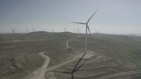 تصوير درون جوي لحقول توربينات الرياح وطواحين الهواء وسط الرمال الذهبية في المناطق الصحرواية، توليد الكهرباء بواسطة مزارع الرياح، مناخ قاسٍ وجاف، مفهوم استخدام الطاقات المتجددة صديقة البيئة، التنمية المستدامة بالطاقة البديلة في دومه الجندل بالمملكة العربية السعودية
