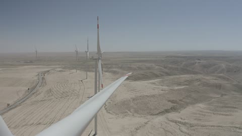 The concept of using renewable energies that are environmentally friendly, sustainable development with alternative energy in Dumat al-Jandal in the Kingdom of Saudi Arabia, generating electricity through wind farms, a harsh and dry climate, aerial drone photography of wind turbine fields and windmills amidst the golden sands in desert areas.