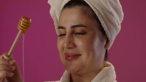 اتباع حمية غذائية، استخدام المنتجات الطبيعية للعناية بالبشرة، ايماءات السرور و السعادة، منتج وطني محلي سعودي، بورتريه لمرأة عربية خليجية سعودية ترتدي روب حمام و منشفة بيضاء تحمل بيدها ملعقة خشبية مغمورة بالعسل، خلفية بنفسجية