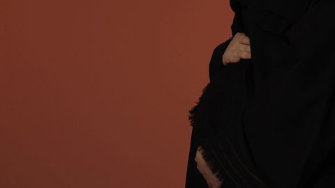 الربت على البطن برفق, مشاعر الامومة و حضن طفلها، مفهوم الحمل والانجاب، الاهتمام بصحة الجنين، بورتريه مقرب لإمرأة عربية خليجية سعودية ترتدي عباءة سوداء تضع يدها على بطنها, خلفية بني