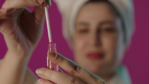 التسويق لمنتجات التجميل, الشغف بوضع المكياج, مفهوم التزين و التجمل, الاهتمام و العناية بالبشرة و الجمال, خلفية غير واضحة لمرأة عربية خليجية سعودية تمسك بأحمر الشفاه, استعمال المستحضرات التجميلية