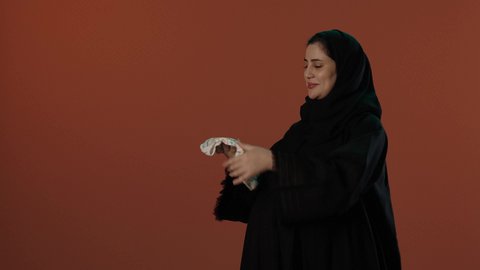 ملابس نوم للأطفال، الاستعداد لاستقبال المولود الجديد, اختيار لبس مواليد رضع، مفهوم الحمل والانجاب، بورتريه لإمرأة عربية خليجية سعودية محجبة ترتدي عباءة سوداء تمسك بيدها افرول، خلفية بني