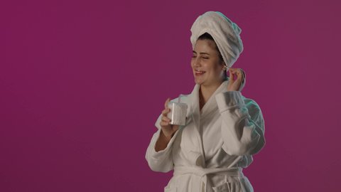روتين نظافة الأذن اليومية, استخدام أعواد و نكاشات القطن، الاعتناء بالنفس و النظافة, بورتريه لامرأة عربية خليجية سعودية مبتسمة ترتدي روب حمام و منشفة بيضاء تستخدم نكاشة قطنية, الاهتمام بالمظهر الخارجي, خلفية بنفسجية