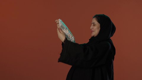 الأمومة و بداية حياة جديدة، اختيار ملابس مواليد رضع، مفهوم الحمل والانجاب، بورتريه لإمرأة عربية خليجية سعودية محجبة ترتدي عباءة سوداء تمسك بيدها افرول، خلفية بني