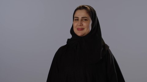 القبول و الموافقة و الرضا، تعابير وجه و يدين تدل على الاعجاب، التعبير عن الاتقان، بورتريه لامرأة عربية خليجية سعودية محجبة ترتدي عباءة سوداء ترفع اصبع الابهام لاعلى باشارة اللايك, خلفية رمادية