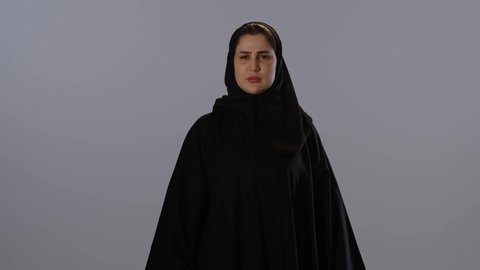 تعابير الحزم والجدية, طلب التوقف و عدم الاقتراب, مفهوم الرفض و الامتناع و الانزعاج,  بورتريه لامرأة عربيه خليجيه سعودية محجبة ترتدي عباءة سوداء ترفع كف يدها لأعلى، خلفية رمادية