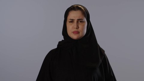 طلب التوقف و عدم الاقتراب, تعابير الحزم و الجدية, مفهوم الرفض و الامتناع و الانزعاج, بورتريه لامرأة عربيه خليجيه سعودية محجبة ترتدي عباءة سوداء ترفع كف يدها لأعلى، خلفية رمادية