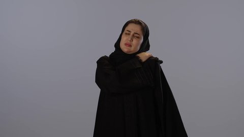 التهابات المفاصل و العظام، مسك الكتف و الخشونة، الإحساس بالمرض و الوجع، طلب المساعدة و الحاجة للعلاج، بورتريه لامرأة عربيه خليجيه سعودية محجبة ترتدي عباءة سوداء, خلفية رمادية