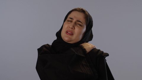 مسك الكتف و الخشونة، مفهوم أمراض و التهابات المفاصل و العظام، الإحساس بالمرض و الوجع، طلب المساعدة و الحاجة للعلاج، بورتريه لامرأة عربيه خليجيه سعودية محجبة ترتدي عباءة سوداء, خلفية رمادية