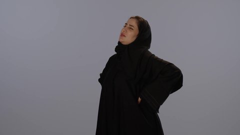 الاحساس بألم في العمود الفقري, التهاب العضلات و المفاصل، بورتريه لامرأة عربيه خليجيه سعودية محجبة ترتدي عباءة سوداء تضع يدها على ظهرها بايماءات التعب،  خلفية رمادية