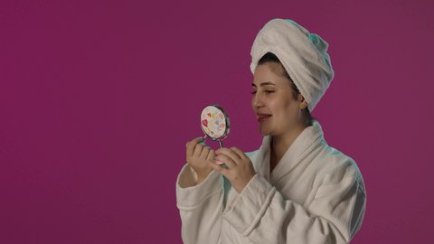 الاهتمام بالبشرة و الجمال, الشغف بوضع المكياج, مفهوم التزين و التجمل, بورترية لمرأة عربية خليجية سعودية تستخدم أحمر الشفاه و تنظر في المرآة، سيدة خبيرة بمستحضرات التجميل, العناية بالنفس و الاطلالة المتألقة,  ايماءات السرور و السعادة، خلفية بنفسجية