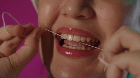 تجنب التسوس و أمراض اللثة، التأكد من نظافة الأسنان بعد تناول الطعام, بورتريه مقرب لامرأة عربية خليجية سعودية تقوم بالتنظيف باستعمال الخيط السني, روتين نظافة الفم اليومية، خلفية بنفسجية