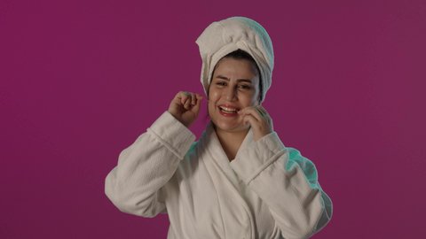 روتين نظافة الفم اليومية، التأكد من نظافة الأسنان بعد تناول الطعام, بورتريه لامرأة عربية خليجية سعودية  ترتدي روب حمام و منشفة بيضاء تقوم بالتنظيف باستعمال الخيط السني, تجنب التسوس و أمراض اللثة, خلفية بنفسجية