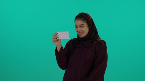 ام تحادث جنينها من خلال صورة السونار باللون الابيض والاسود، مفهوم الحمل والانجاب، الاهتمام بصحة الجنين، الحفاظ على صحتها و صحة طفلها، الاستفادة من العروض الموسمية والتخفيضات، تصوير مقرب لإمراة عربية خليجة سعودية ترتدي العباءة والحجاب  بتعابير السرور، خلفية زرقاء