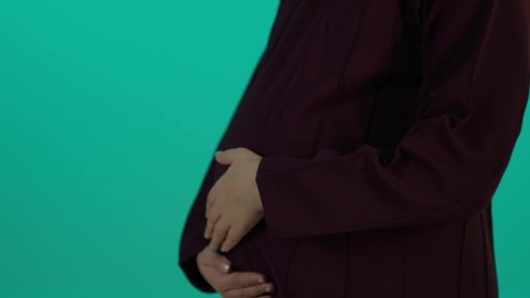 حنان الام وحضن طفلها داخل بطنها، مفهوم الحمل والانجاب، الاهتمام بصحة الجنين، الحفاظ على صحتها و صحة طفلها، الاستفادة من العروض الموسمية والتخفيضات، تصوير مقرب لإمراة عربية خليجة سعودية ترتدي العباءة والحجاب  بتعابير السرور، خلفية زرقاء