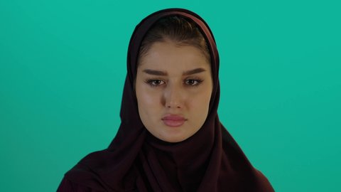 الام الحامل تفرض التوقف، مفهوم الحمل والانجاب، الاهتمام بصحة الجنين، الحفاظ على صحتها و صحة طفلها، إمرأة عربية خليجية سعودية تمسك بيدها حذاء أطفال، تصوير مقرب لإمراة عربية خليجة سعودية ترتدي العباءة والحجاب تنظر إلى الكاميرا بإيماءات الغضب، خلفية زرقاء