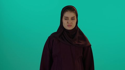 فرض طلب التوقف من الام الحامل، مفهوم الحمل والانجاب، الاهتمام بصحة الجنين، الحفاظ على صحتها و صحة طفلها، إمرأة عربية خليجية سعودية تمسك بيدها حذاء أطفال، تصوير مقرب لإمراة عربية خليجة سعودية ترتدي العباءة والحجاب تنظر إلى الكاميرا بإيماءات الغضب، خلفية زرقاء