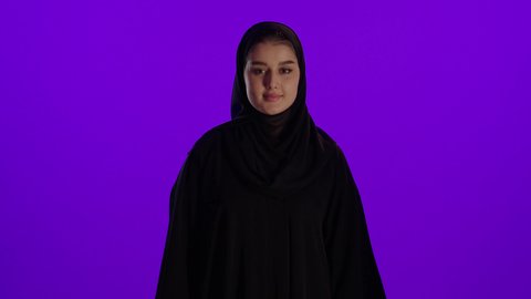 اشارة اصبع الابهام والقبول، مفهوم الحمل والانجاب، الاهتمام بصحة الجنين، الحفاظ على صحتها و صحة طفلها، جمال الأمومة وبداية حياة جديدة، تصوير مقرب لإمراة عربية خليجة سعودية ترتدي العباءة والحجاب تنظر إلى الكاميرا بإيماءات السرور، خلفية بنفسجي