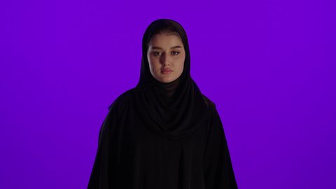 خفض الابهام للاسفل وعدم القبول، مفهوم الحمل والانجاب، الاهتمام بصحة الجنين، الحفاظ على صحتها و صحة طفلها، جمال الأمومة وبداية حياة جديدة، تصوير مقرب لإمراة عربية خليجة سعودية ترتدي العباءة والحجاب تنظر إلى الكاميرا بإيماءات الغضب، خلفية بنفسجي