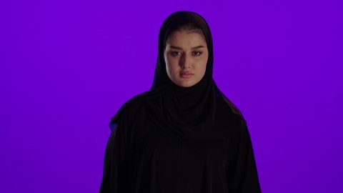 تعابير الغضب وطلب التوقف، مفهوم الحمل والانجاب، الاهتمام بصحة الجنين، الحفاظ على صحتها و صحة طفلها، جمال الأمومة وبداية حياة جديدة، تصوير مقرب لإمراة عربية خليجة سعودية ترتدي العباءة والحجاب تنظر إلى الكاميرا بإيماءات التفكير، خلفية بنفسجي
