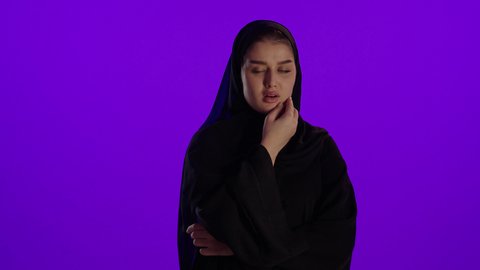 المعاناة من الم الاسنان خلال الحمل، مفهوم الحمل والانجاب، الاهتمام بصحة الجنين، الحفاظ على صحتها و صحة طفلها، جمال الأمومة وبداية حياة جديدة، تصوير مقرب لإمراة عربية خليجة سعودية ترتدي العباءة والحجاب تنظر إلى الكاميرا بإيماءات التفكير، خلفية بنفسجي