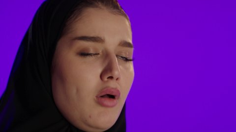 السعال وضيق التنفس، مفهوم الحمل والانجاب، الاهتمام بصحة الجنين، الحفاظ على صحتها و صحة طفلها،جمال الأمومة وبداية حياة جديدة، تصوير مقرب لإمراة عربية خليجة سعودية ترتدي العباءة والحجاب تنظر إلى الكاميرا بإيماءات التفكير، خلفية بنفسجي