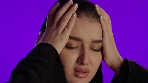 آلام الرأس عند الام الحامل، مفهوم الحمل والانجاب، الاهتمام بصحة الجنين، الحفاظ على صحتها و صحة طفلها، جمال الأمومة وبداية حياة جديدة، تصوير مقرب لإمراة عربية خليجة سعودية ترتدي العباءة والحجاب تنظر إلى الكاميرا بإيماءات التفكير، خلفية بنفسجي