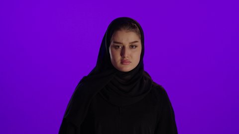 طلب التوقف والغضب الام الحامل، مفهوم الحمل والانجاب، الاهتمام بصحة الجنين، الحفاظ على صحتها و صحة طفلها، جمال الأمومة وبداية حياة جديدة، تصوير مقرب لإمراة عربية خليجة سعودية ترتدي العباءة والحجاب تنظر إلى الكاميرا بإيماءات التفكير، خلفية بنفسجي