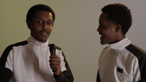 تعابير الاندماج والسرور بالاستماع الى الموسيقى، قضاء وقت ممتع بأداء العروض الصوتية، بورتريه لطالبان توأم ذو بشرة سمراء عربيان خليجيان سعوديان يرتديان اليونيفورم المدرسى، خلفية بيج