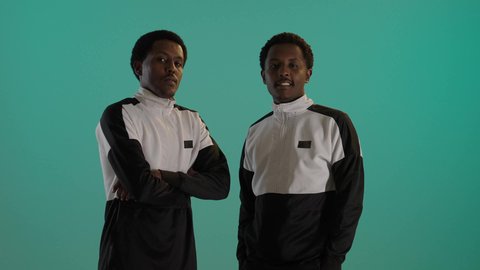 الوقوف باستقامة وأيدي متقاطعة، تعابير وايماءات الثقة بالنفس، بورتريه لطالبان توأم ذو بشرة سمراء عربيان خليجيان سعوديان يرتديان اليونيفورم المدرسى، خلفية حضراء